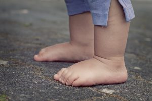 Bild: Füße eines Babys ohne Hausschuhe, wie Pantoletten, Sandalen, Clogs, Barfußschuhe etc., in der Seitenansicht - stehend auf einer Straße. Interner Link zu Hausschuhe für Kinder.